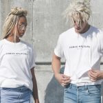 man and woman in white-and-gray force majeure-printed crew-neck t-shirts standing near gray concrete wall