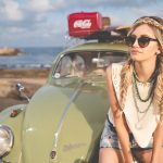 selective focus photography of woman sitting on Volkswagen Beetle parked on beach shore