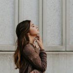 woman in brown long-sleeved top standing beside wall