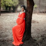 a woman in an orange dress leaning against a tree