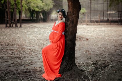 a woman in an orange dress leaning against a tree